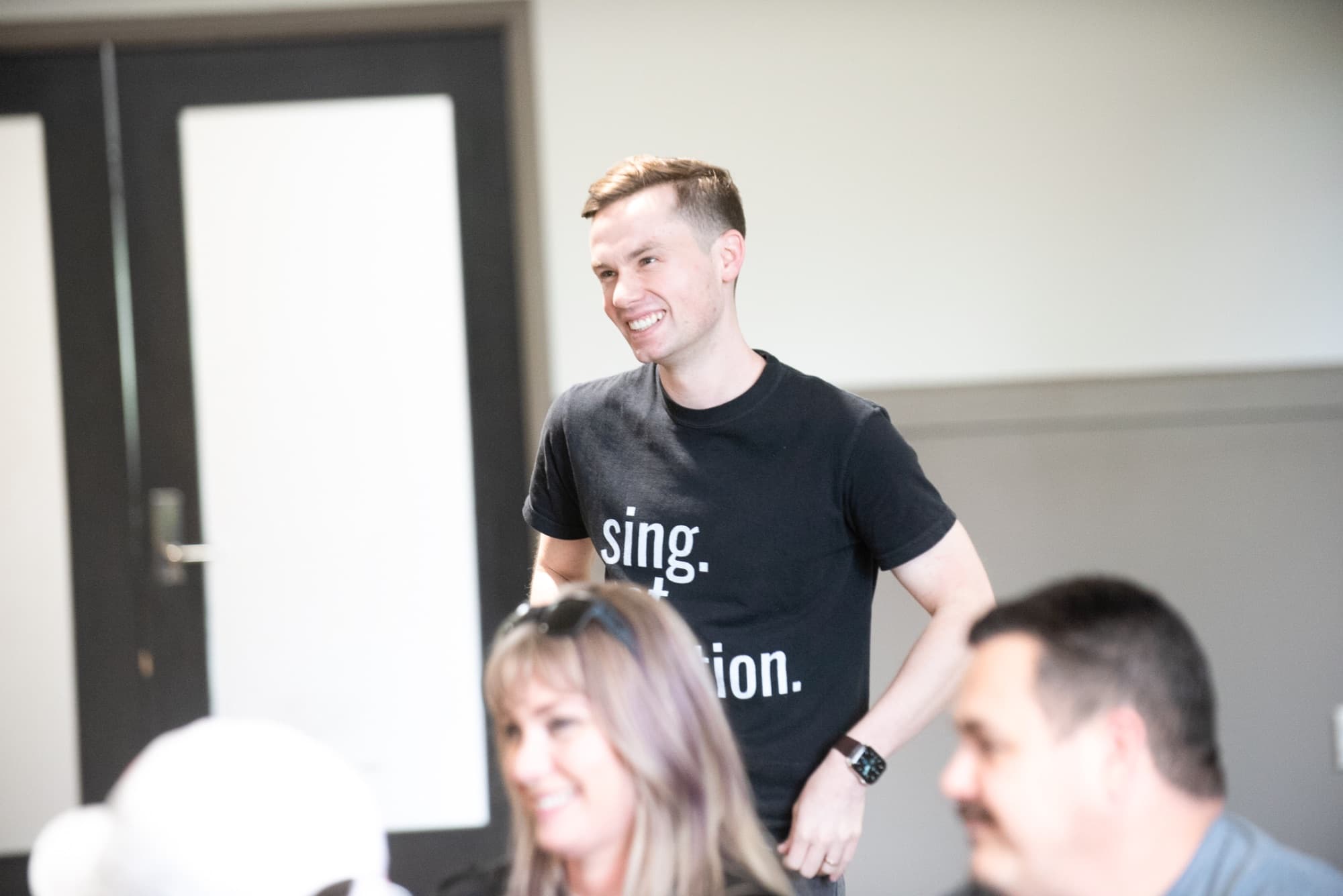 Man in black tee smiling while leading a group class or workshop in a bright studio space